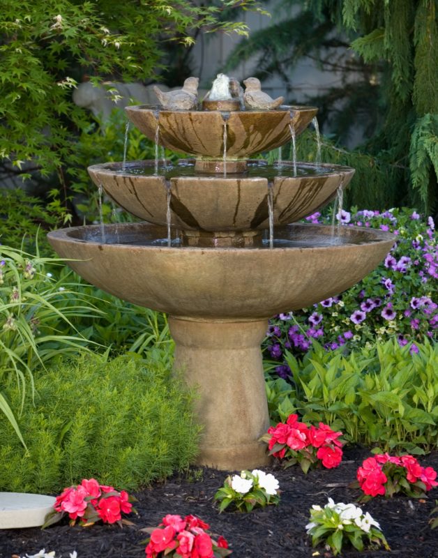 three-tiered stone tranquility fountain with sculpture birds in garden of flowers