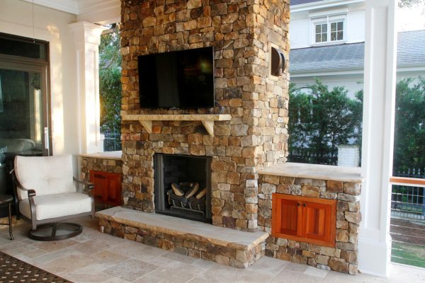 stone fireplace with raised hearth and side cabinets with TV mounted over a stone mantel in a sunroom