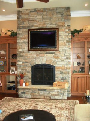 stone fireplace with raised hearth, TV inset into wall above, flanked by wooden bookcases