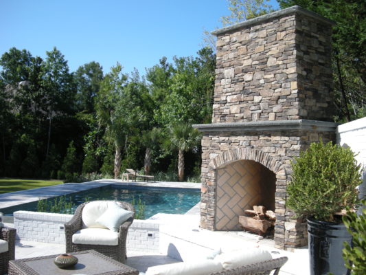 large, outdoor living room with fireplace and swimming pool