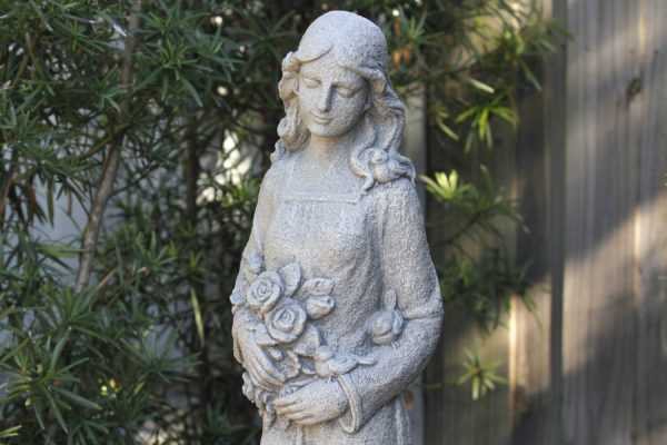 stone garden art sculpture of a lady holding flowers and birds