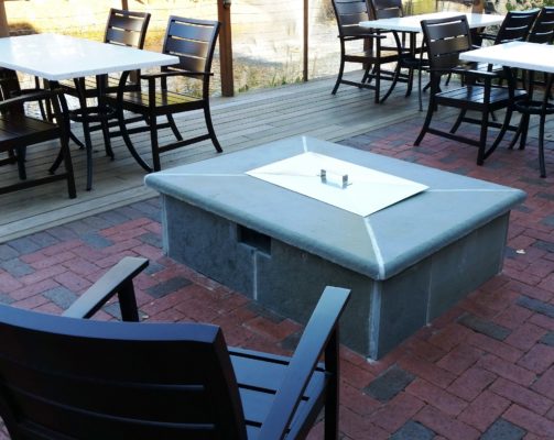 oblong stone lidded fire pit on a stone patio amongst dining tables and chairs at a restaurant