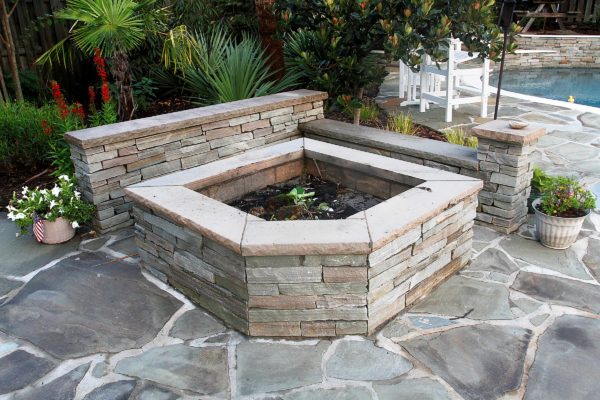 square stone fire pit and seating wall on a flagstone patio by a swimming pool