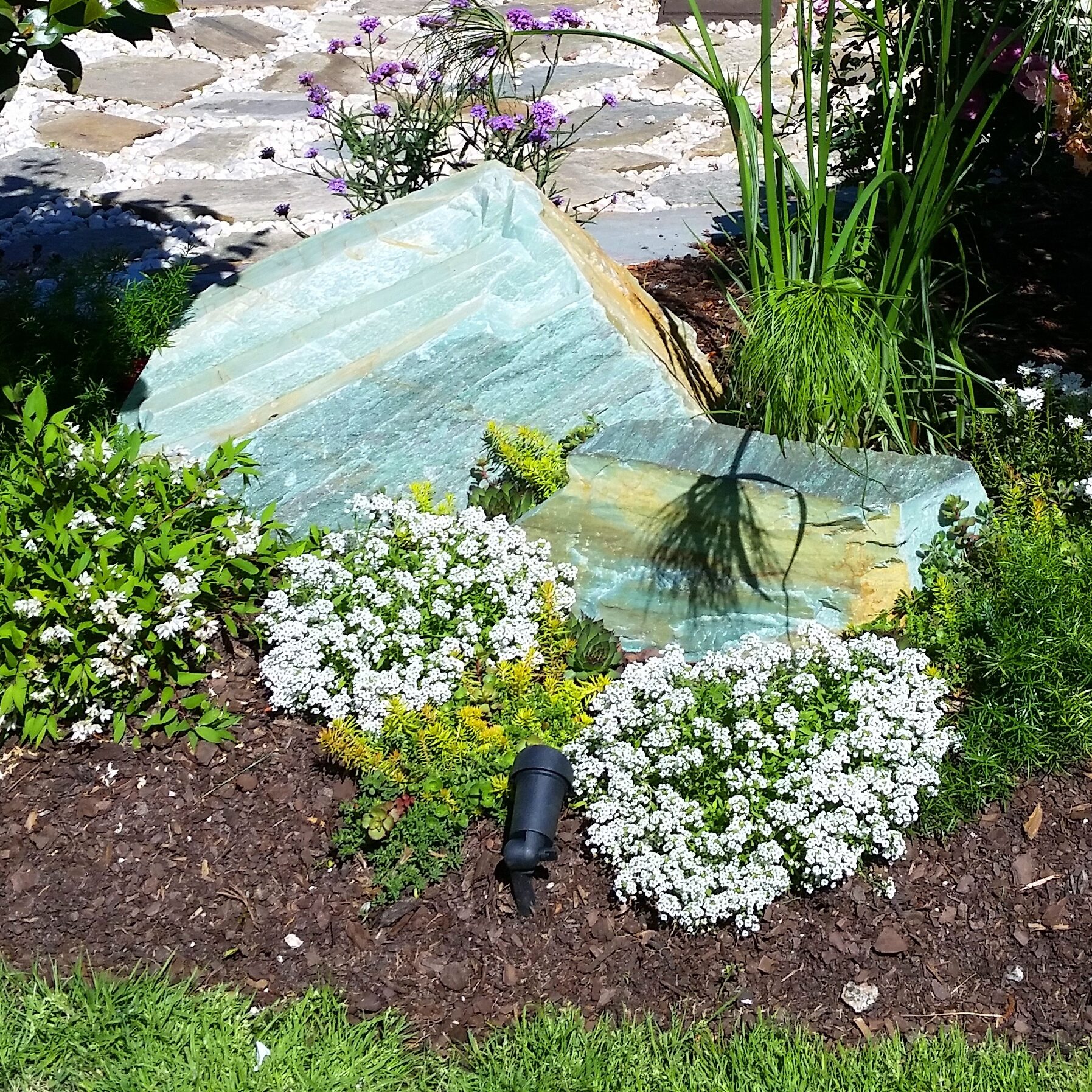 large turquoise green stone boulder in a garden with flowers