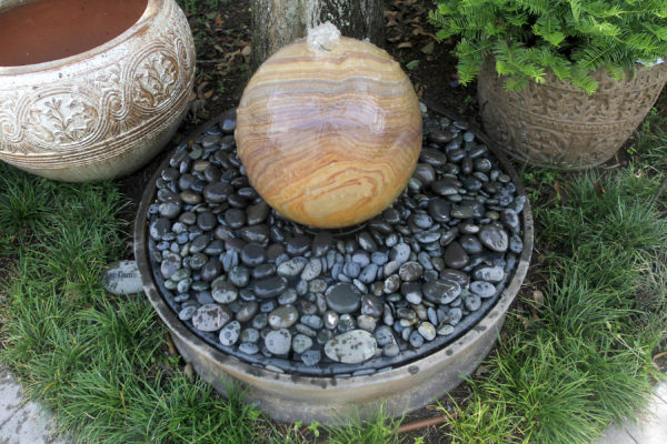 spherical rainbow fountain bubbling water into a ring of black mexican beach pebbles at stone garden