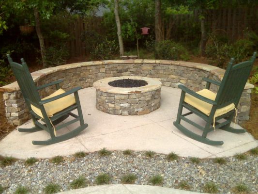 round stone fire pit and seating wall on patio with rocking chairs in garden