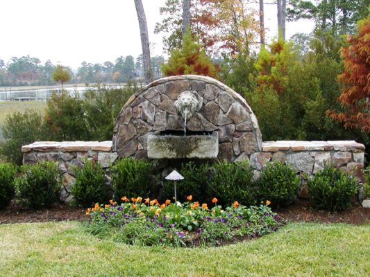 stone garden fountain featuring lion's head in a garden with colorful flowers