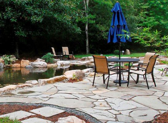 flagstone patio and pathway by a pond in a garden with outdoor living and dining areas