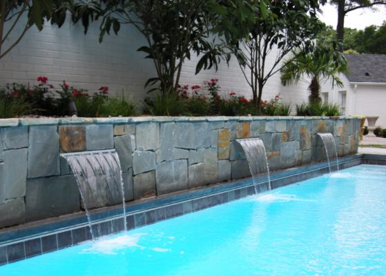 stone garden wall fountains spilling into swimming pool in backyard outdoor living area