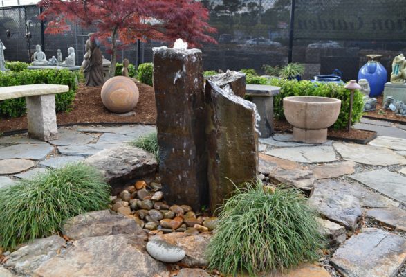 triple basalt column disappearing fountain bubbling water into a ring of beach pebbles on a stone patio at inspiration garden display