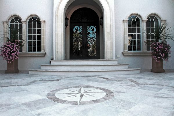 stone patio featuring a compass star design at the front door entrance of a grand, stone house
