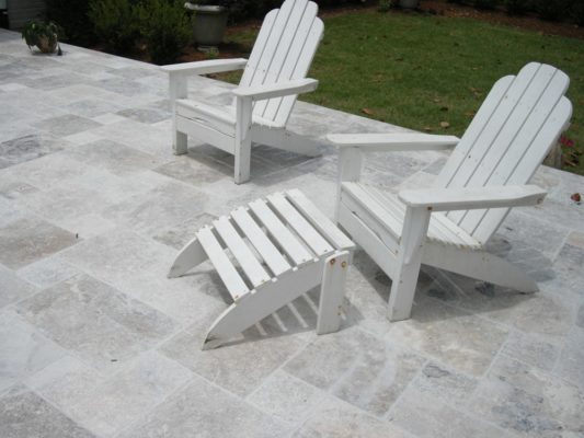 white Adirondack chairs on a silver gray stone patio by a green lawn