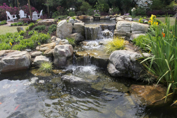 natural-looking stone garden pond with waterfall, koi fish and greenery by outdoor living patio seating area