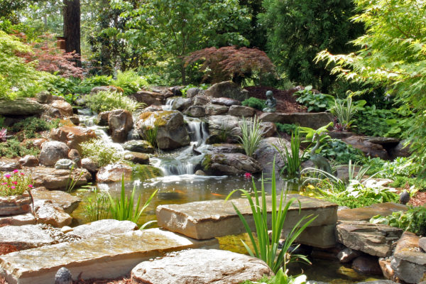 natural-looking stone garden pond with waterfall, koi fish, stone bridge, garden art and greenery