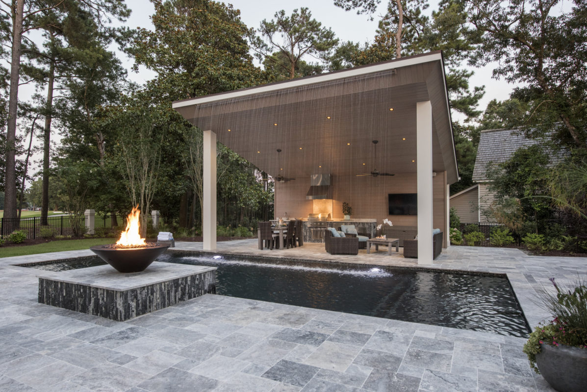outdoor kitchen and living room featuring fire bowl on stone patio and waterfall feature
