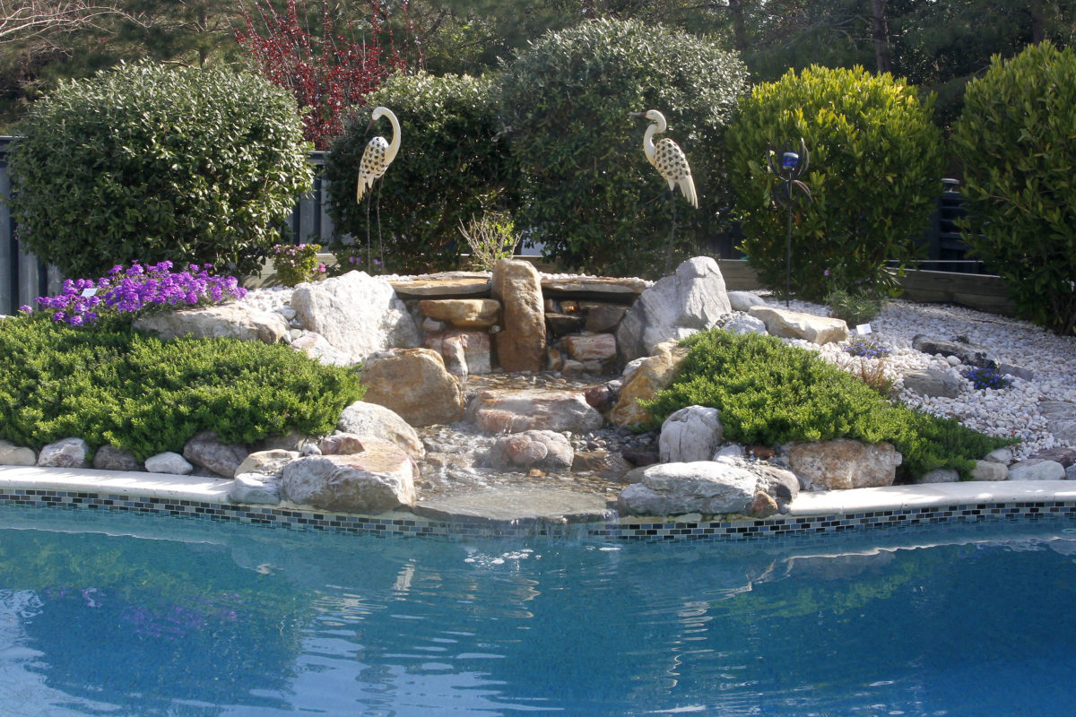 stone garden fountain cascading into a swimming pool with bird garden art, gravel and flowers