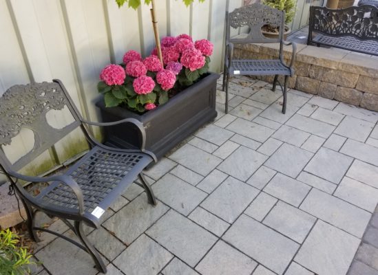 stone pavers patio, stone wall, chairs, and plant pot at stone garden display