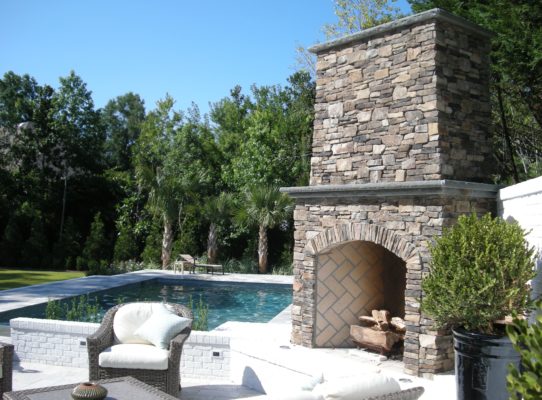 outdoor living room featuring stone patio, stone fireplace and swimming pool