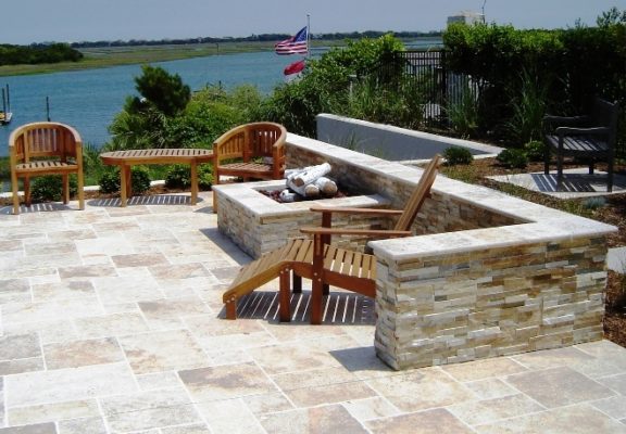 stone outdoor living patio with square fire-pit and seating wall overlooking waterway