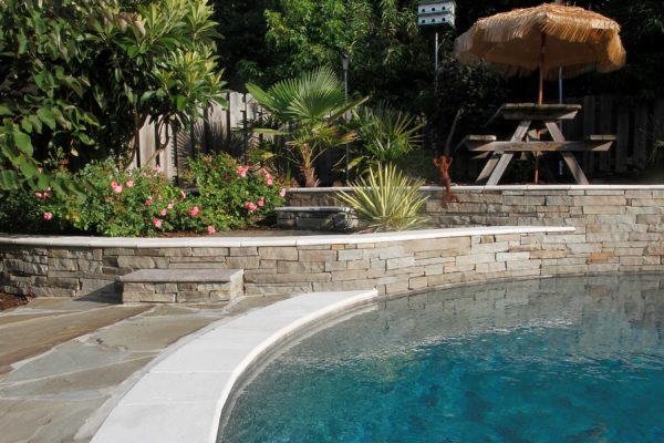 outdoor living area featuring raised stone patio, terraced garden and pool