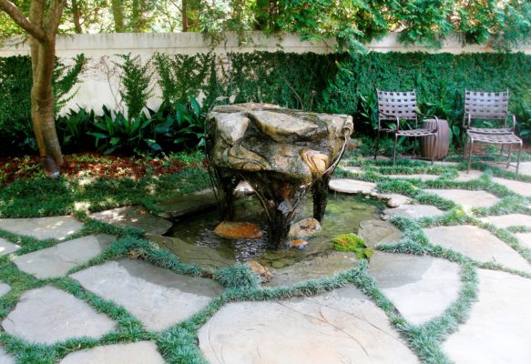 private outdoor living area with flagstone patio, creative water fountain, chairs and a garden wall covered in green foliage