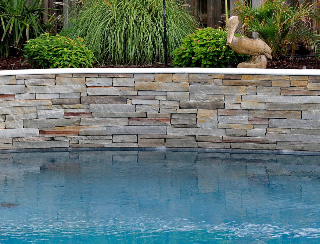 stone retaining wall by a swimming pool with pelican garden art statue