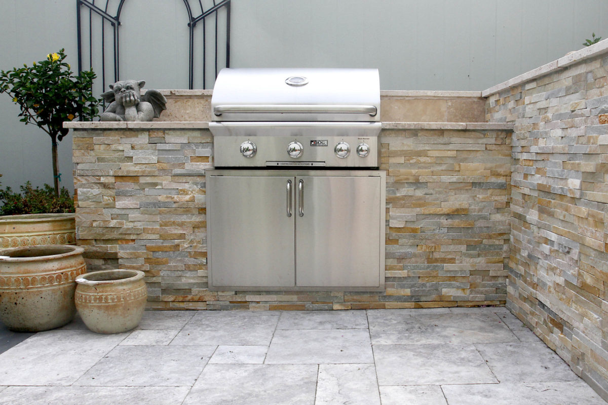 stone, outdoor living kitchen, grill cabinet with garden art and plant pots on a stone patio at stone garden display