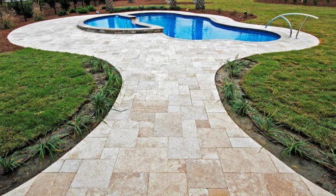 travertine tile pathway and swimming pool surround in green garden