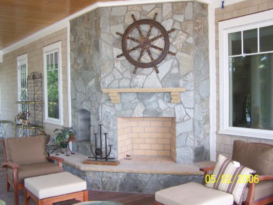 large outdoor stone fireplace with raised hearth on a back porch