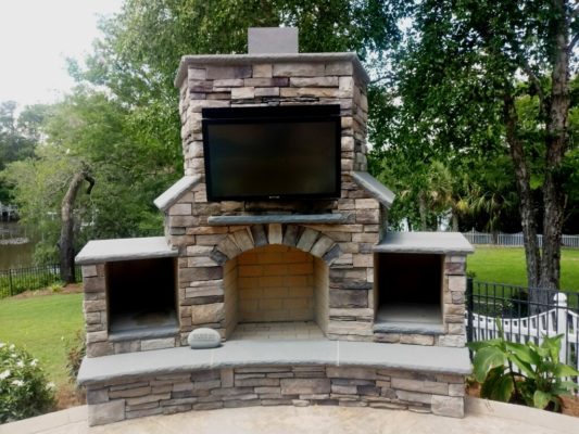 large, stone outdoor fireplace with television for outdoor living