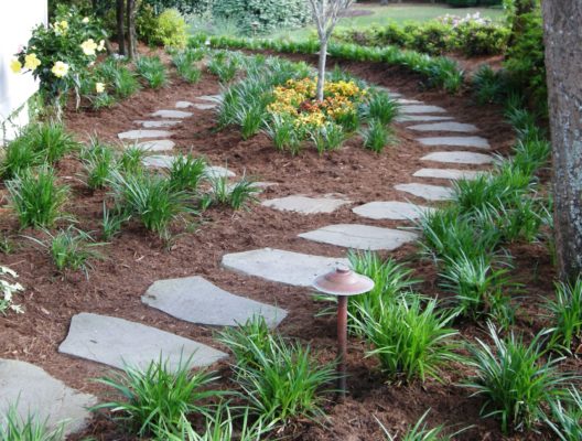 stepping stone garden pathway nestled in fresh mulch with colorful yellow flowers and foliage