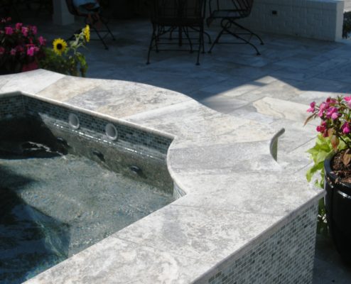 silver travertine stone tiles cap a pool spa on a backyard patio