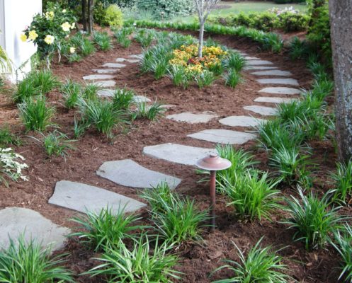stepping stone garden pathway nestled in fresh mulch with flowers and foliage