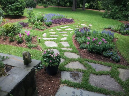 stepping stone garden pathway nestled in green lawn by a colorful garden