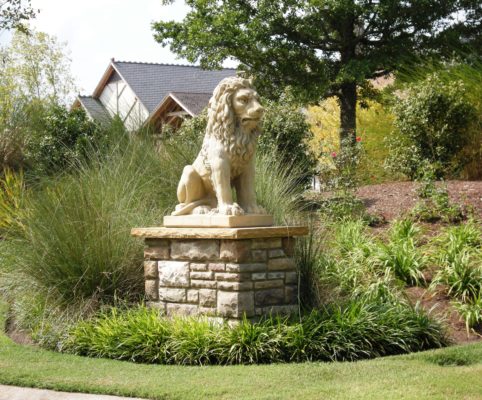 stone pedestal holding a lion art statue in a green garden