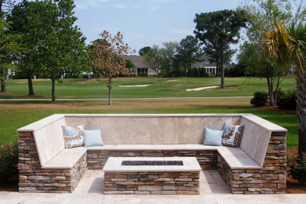 stone outdoor living patio with oblong fire-pit and seating bench overlooking golf course