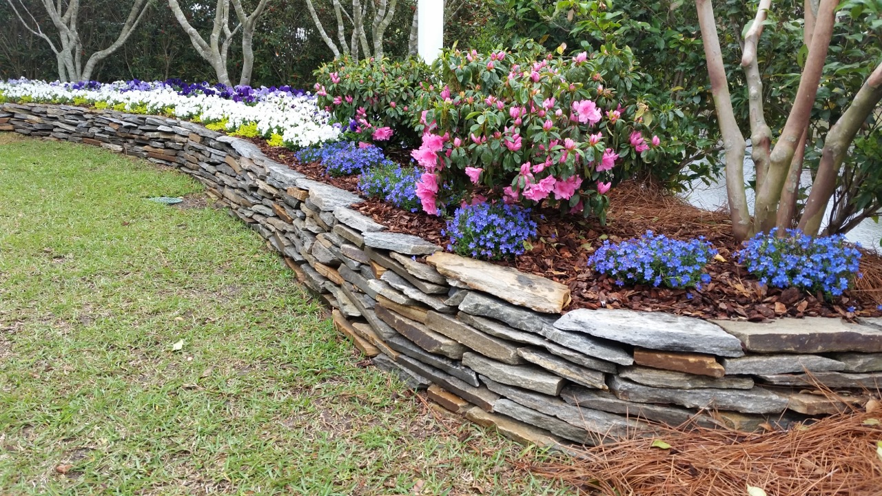 stacked stone wall in a garden of colorful flowers and mulch