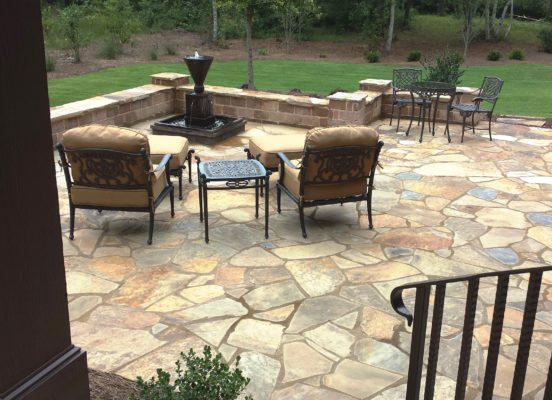 flagstone patio with bubbling fountain and seating wall overlooking garden with outdoor living chairs