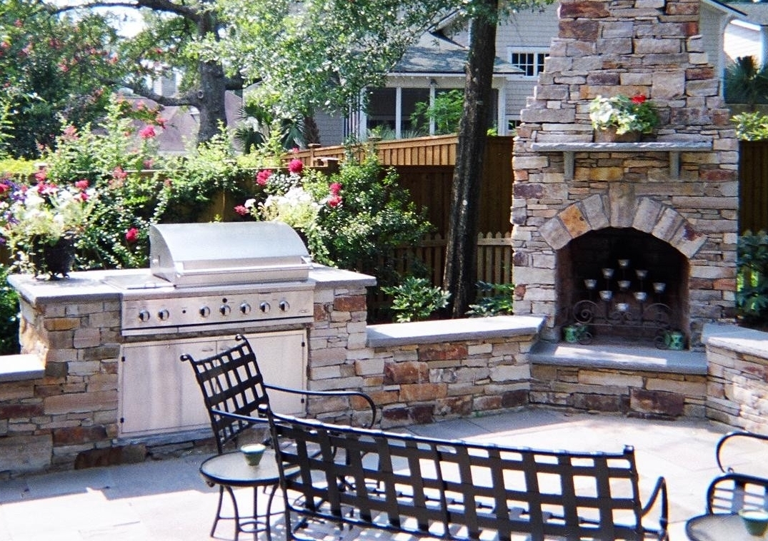 outdoor living room featuring stone fireplace, built-in gas grill and seating walls