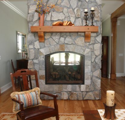 stone indoor double-sided fireplace in a living room with a wooden mantel