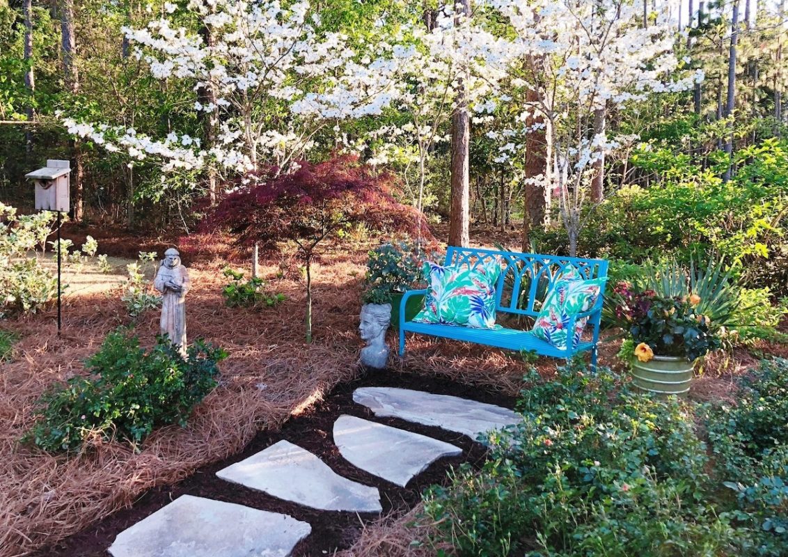stepping stone pathway to a metal bench in a pine straw garden with blossoming trees