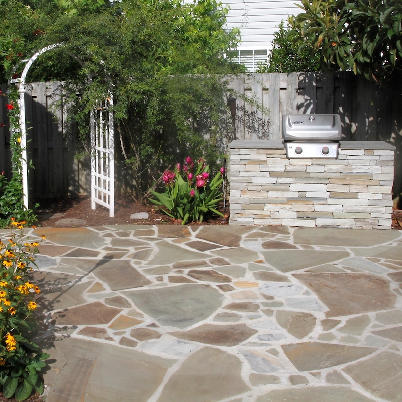 flagstone patio with stone grill station in a backyard garden