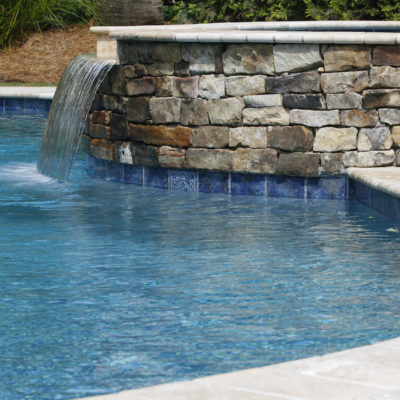 stone spa waterfall into a swimming pool with a travertine coping edge