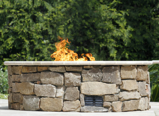 stone gas fire pit with flames on garden patio