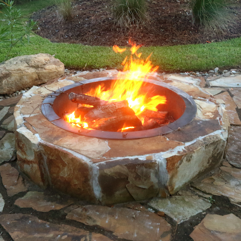 stone fire pit on a flagstone patio in a back yard garden
