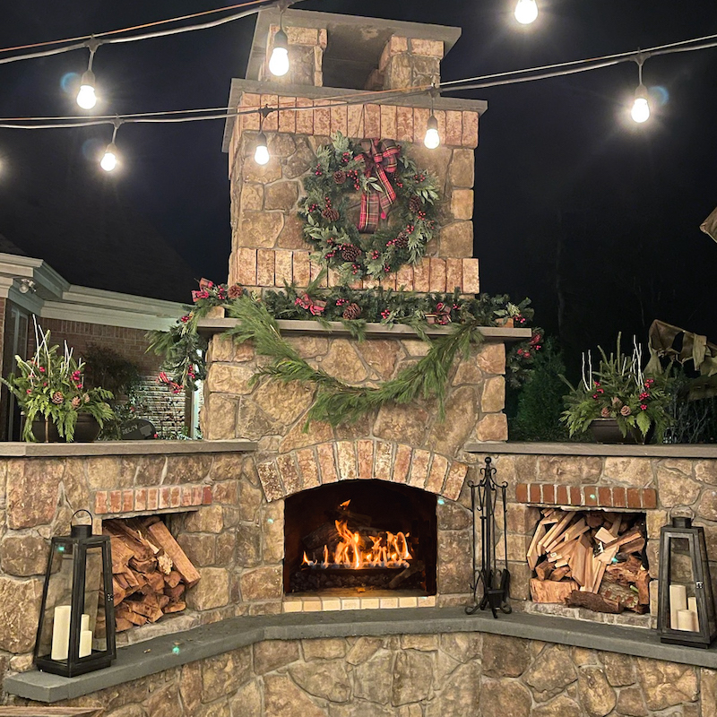 stone outdoor fireplace with fire decorated for Christmas holidays in a wilmington nc back yard