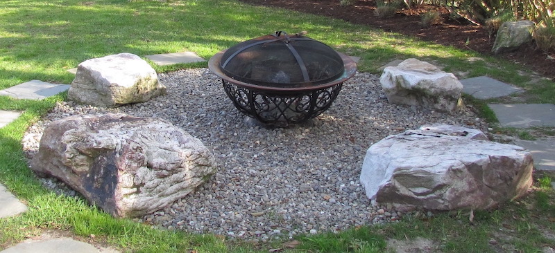metal fire pit bowl in a gravel circle patio with boulders for seats